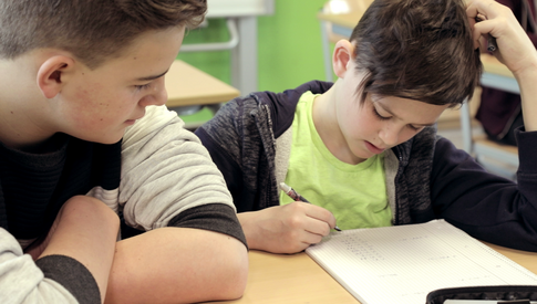 Ein größerer Schüler beobachtet einen kleineren beim Schreiben