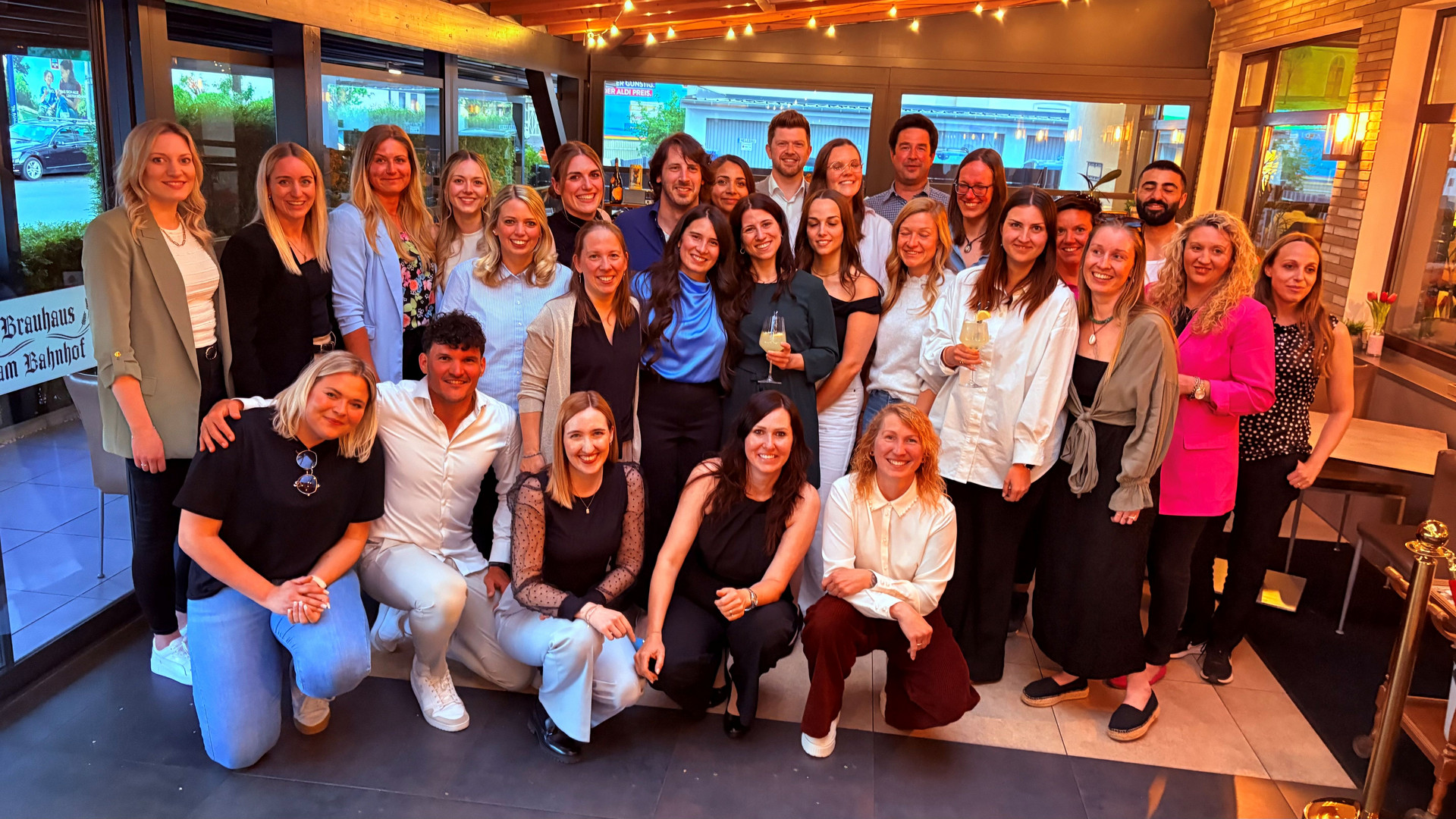 Gruppenfoto der Ausbildungsgruppen F24 & H24 bei der Abschiedsfeier. Zu sehen sind 28 lächelnde Personen, die sich in guter Stimmung in 3 Reihen für das Foto aufgestellt haben.