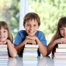 Glückliche Schulkinder mit vielen Büchern sitzend im Klassenzimmer