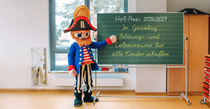 Illustration: Ein Playmobil-Männchen zeigt auf eine Schultafel, auf der das Motto des ausgelobten Preises geschrieben steht