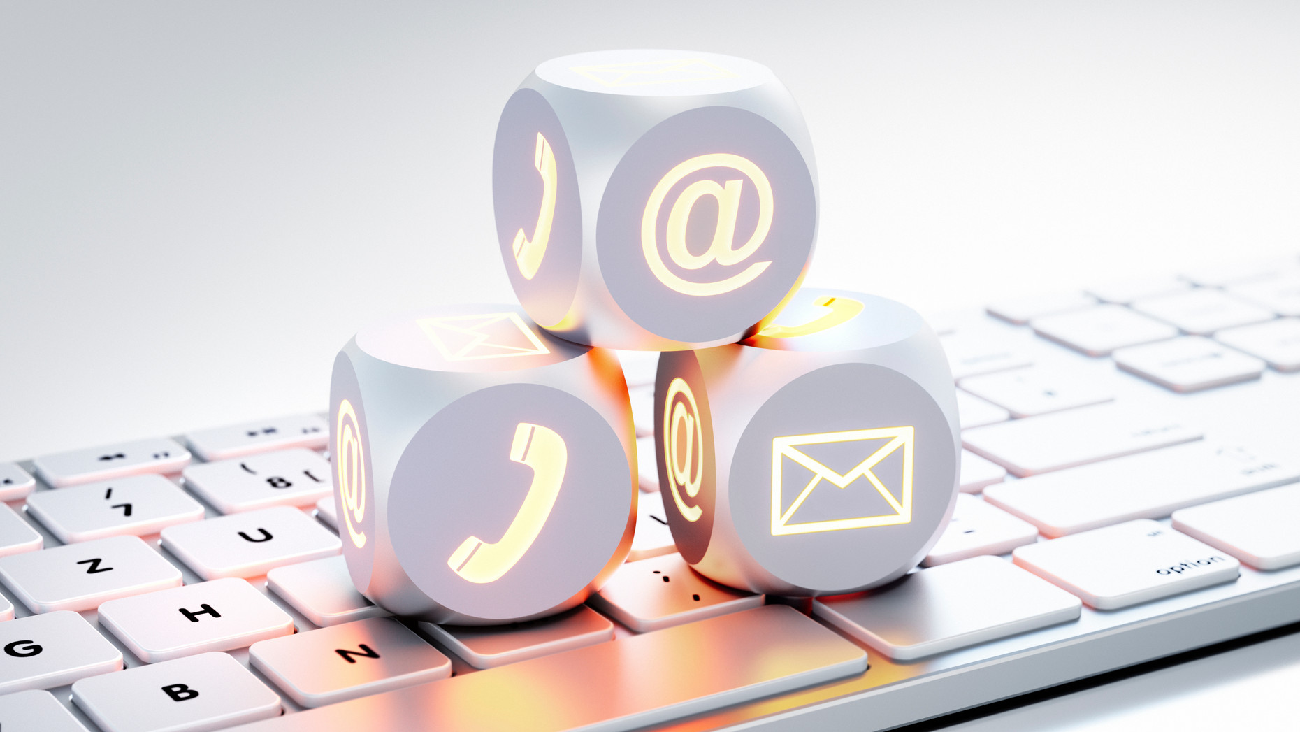 Drei Würfel mit Icons für Kommunikationskanäle wie Brief, Telefon auf einer Tastatur liegend