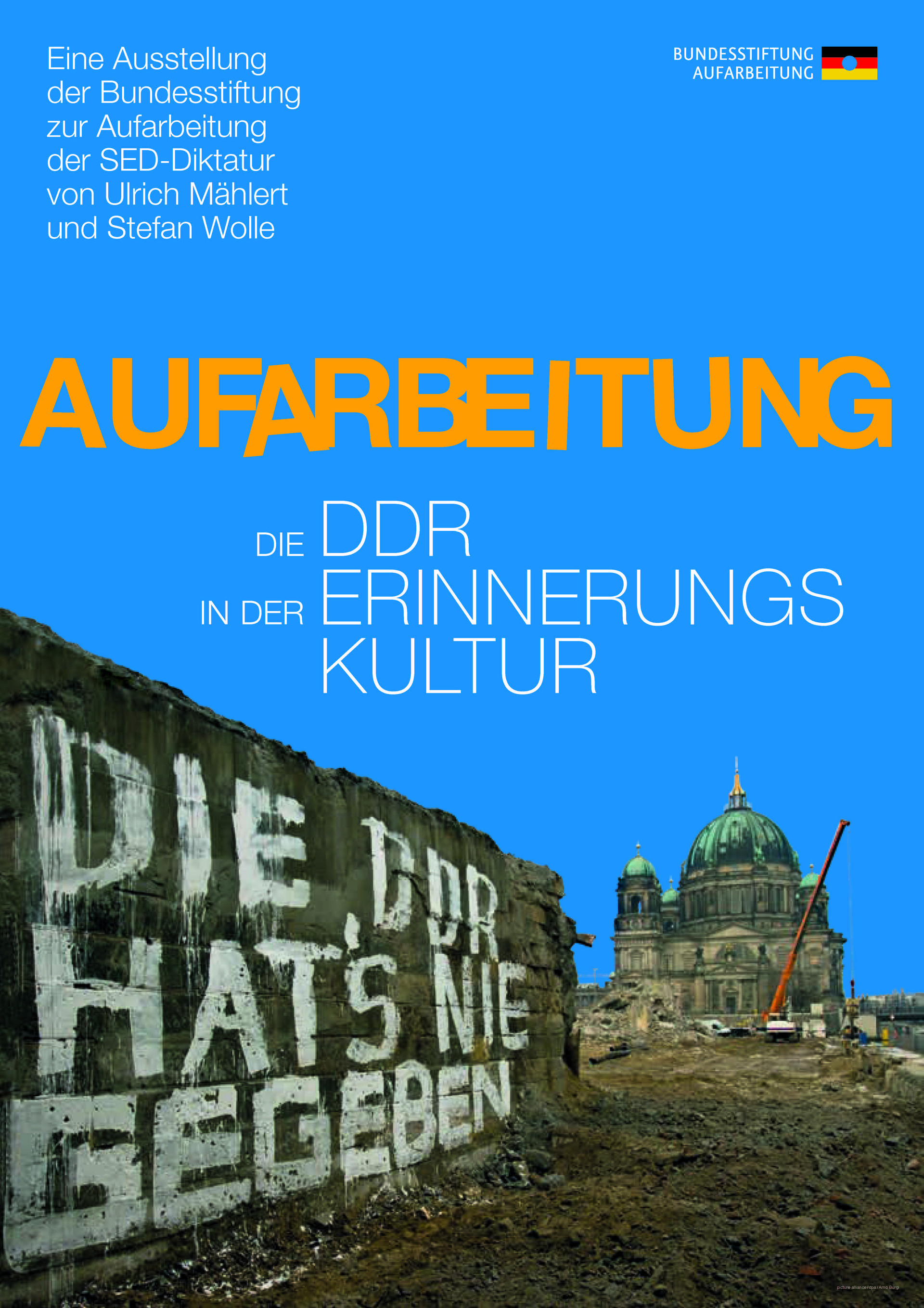 Es zeigt eine Mauer der Brücke Rathausstraße auf der in weißer Farbe geschrieben steht „Die DDR hat´s nie gegeben“. Im Hintergrund ist der Berliner Dom zu sehen, dazwischen die Brache, auf der einst der Palast der Republik gestanden hat.