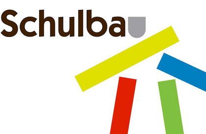 Auf weißem Hintergrund steht oben links das Wort „Schulbau“ in dunkelbrauner Schrift. Daneben ist ein graues Symbol. Darunter sind breite gelbe und blaue Balken schräg angeordnet; zwei schmale rote und grüne Balken verlaufen senkrecht.