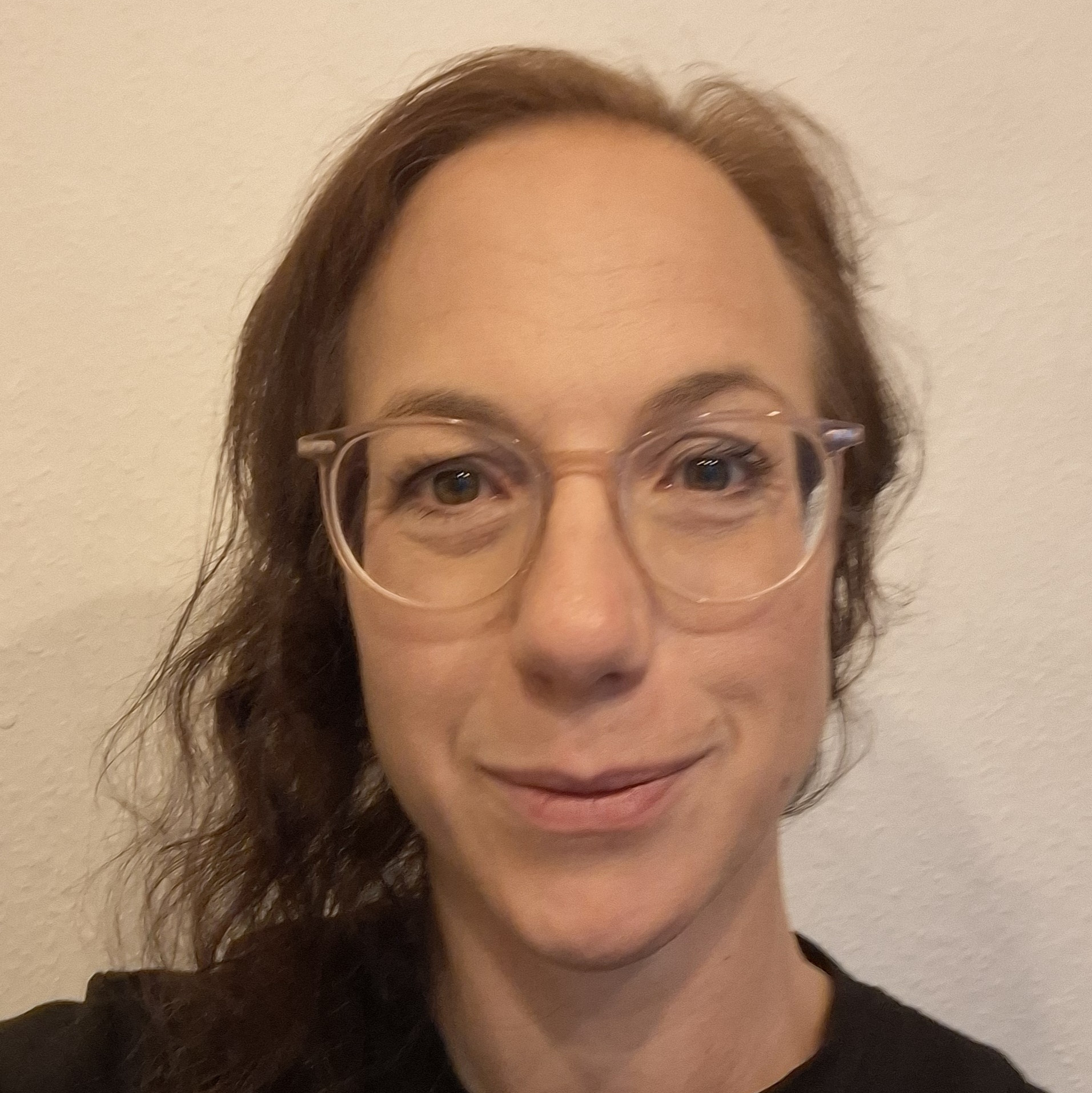 Portrait einer Person mit langen Haaren, Brille und schwarzem Oberteil 