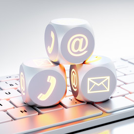 Drei Würfel mit Icons für Kommunikationskanäle wie Brief, Telefon auf einer Tastatur liegend