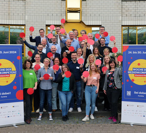 Gruppenbild mit rund 30 Personen mit roten Punkten in der Hand, Roll-ups zur Woche der Medienkompetenz