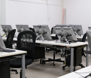 Ein leerer Computerraum mit mehreren Arbeitsplätzen, Monitoren und Stühlen, bereit zur Benutzung.