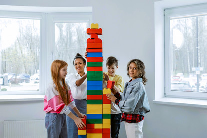 Lehrerin baut gemeinsam mit Schülerinnen und Schülern einen Turm aus Duplo-Steinen