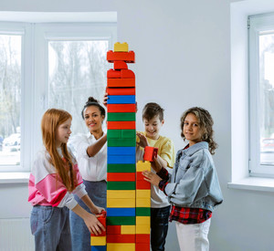 Lehrerin baut gemeinsam mit Schülerinnen und Schülern einen Turm aus Duplo-Steinen