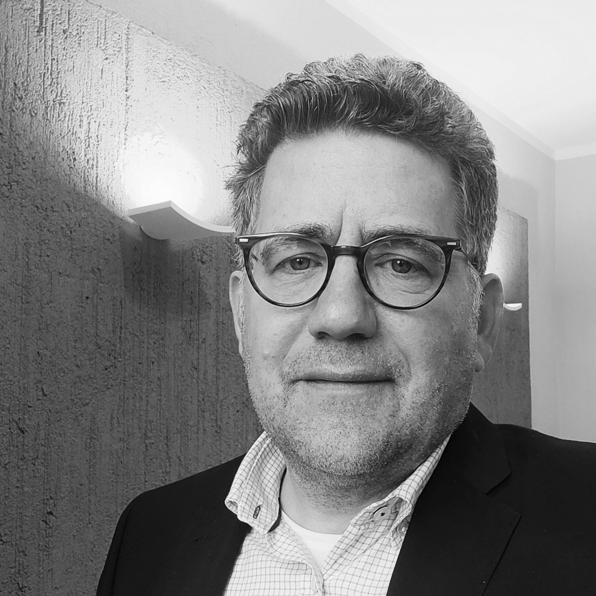 20. LEB Lucas Elvermann Schwarz-weiß Portrait einer Person mit Brille und kurzen Haaren. Die Person trägt ein helles Hemd und ein dunkles Jackett.