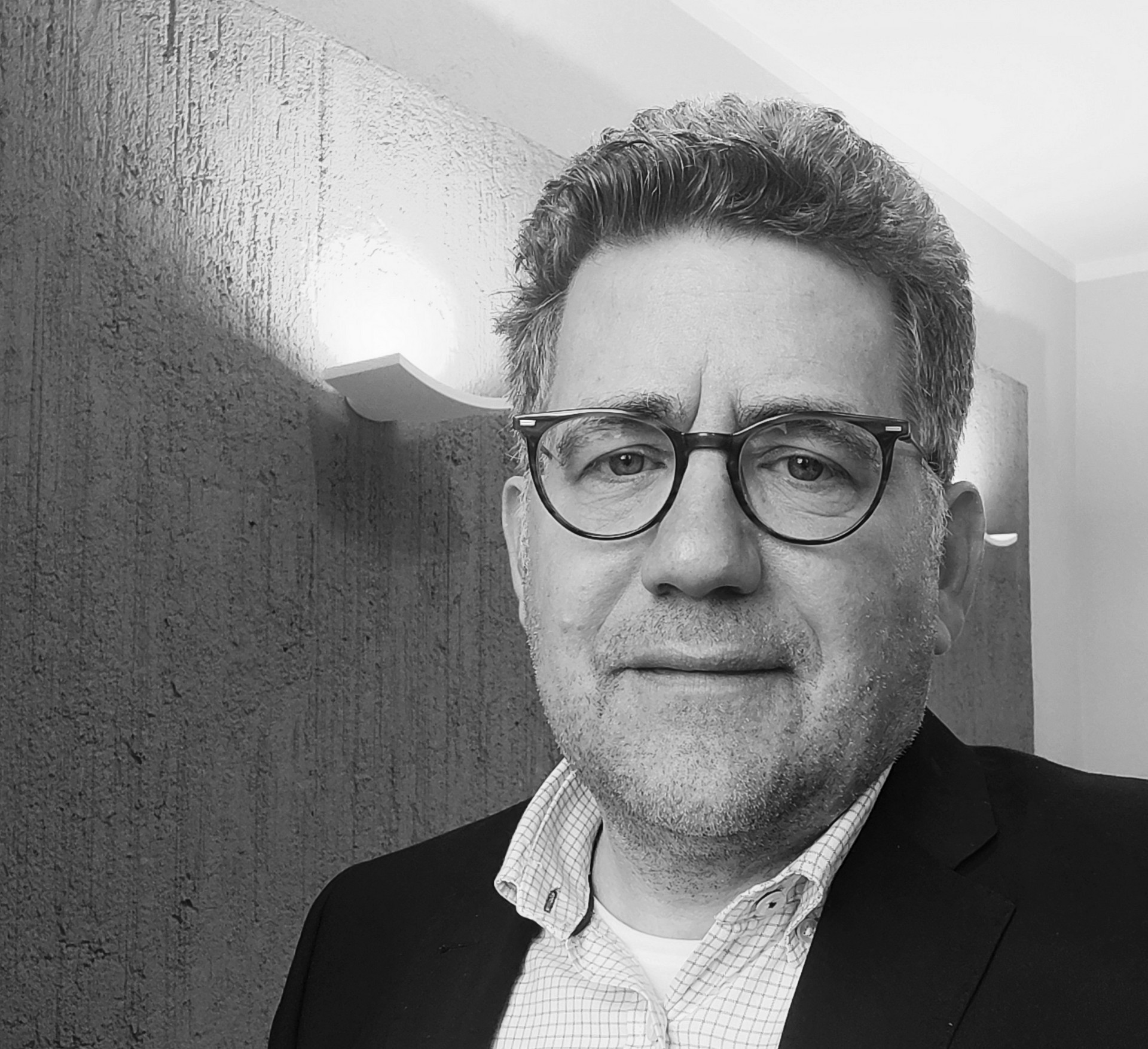 Schwarz-weiß Portrait einer Person mit Brille und kurzen Haaren. Die Person trägt ein helles Hemd und ein dunkles Jackett.