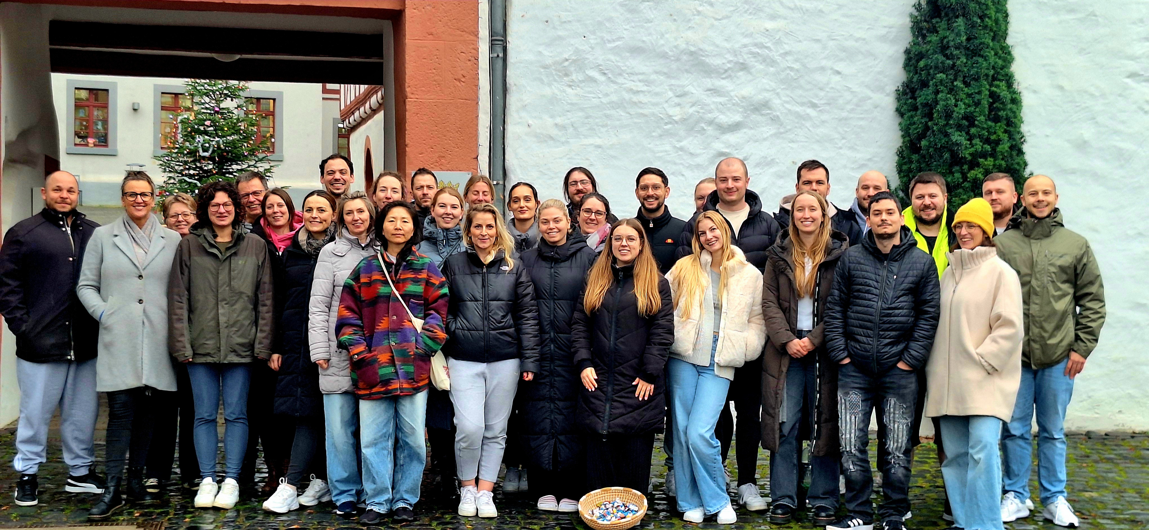 Gruppenfoto der Stammgruppe H25 mit begleitenden Fachleiterinnen und Fachleitern. Die 32 Personen stehen vor dem Eingangstor der Jugendherberge Diez