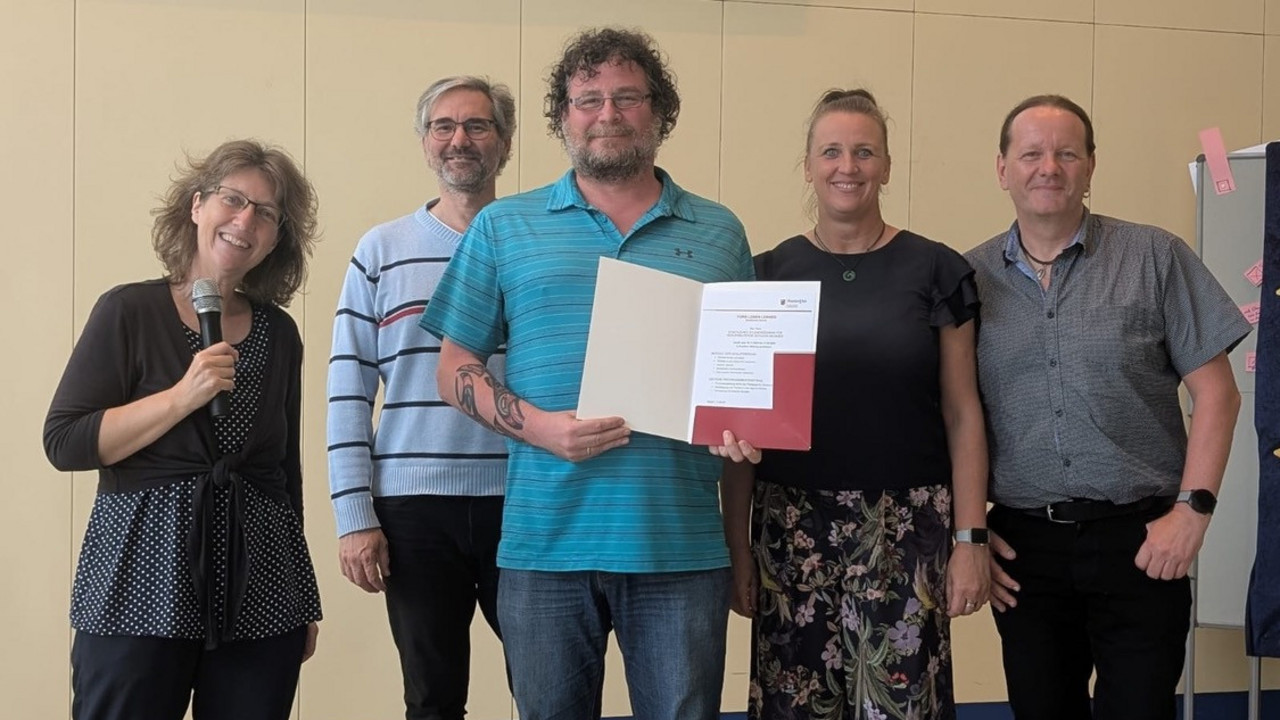Gruppenbild mit 5 Personen. Die mittlere Person hält eine geöffnete Mappe mit einer Urkunde darin.