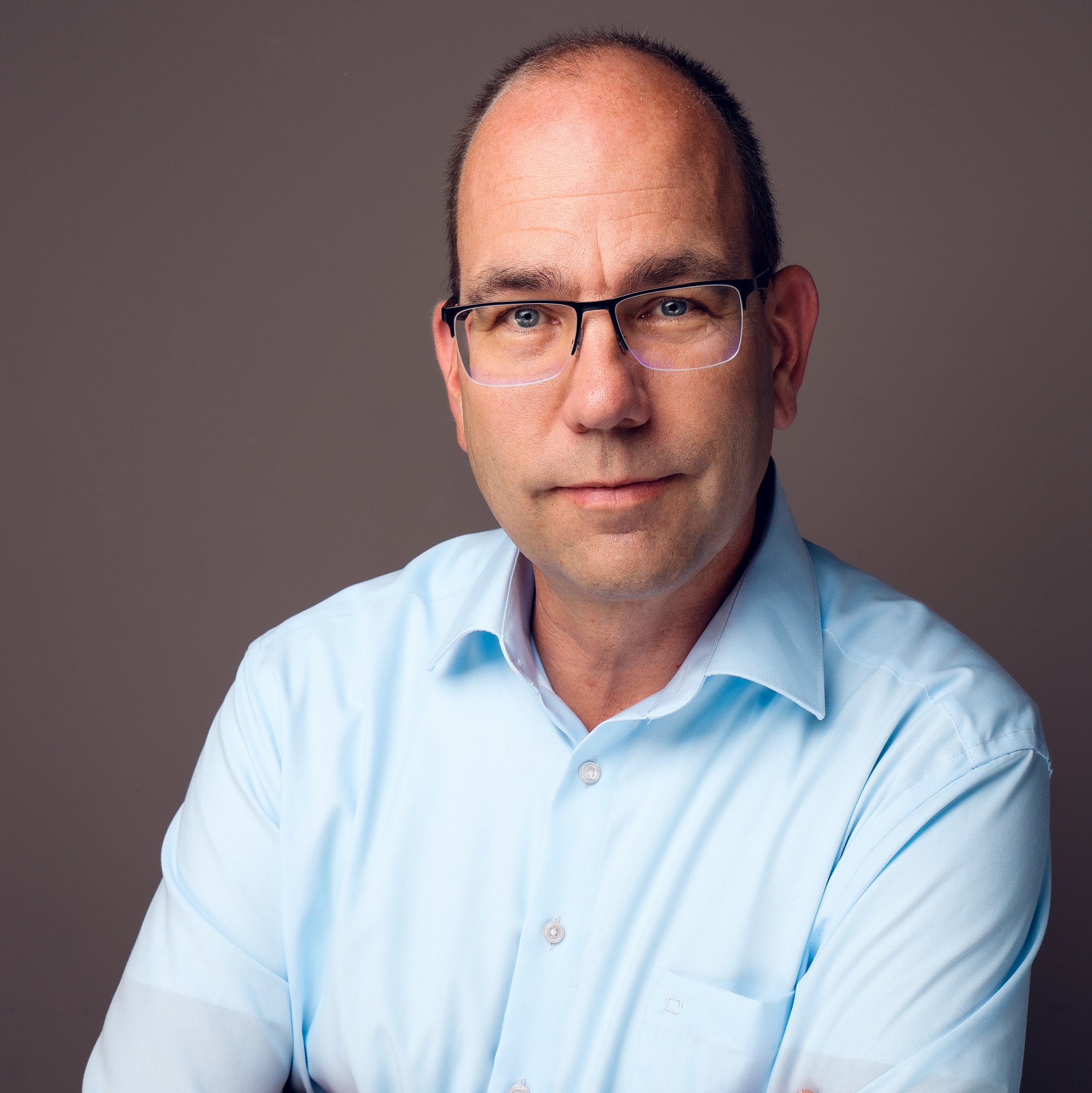 Portrait einer Person mit Brille in hellem Hemd mit locker verschränkten Armen