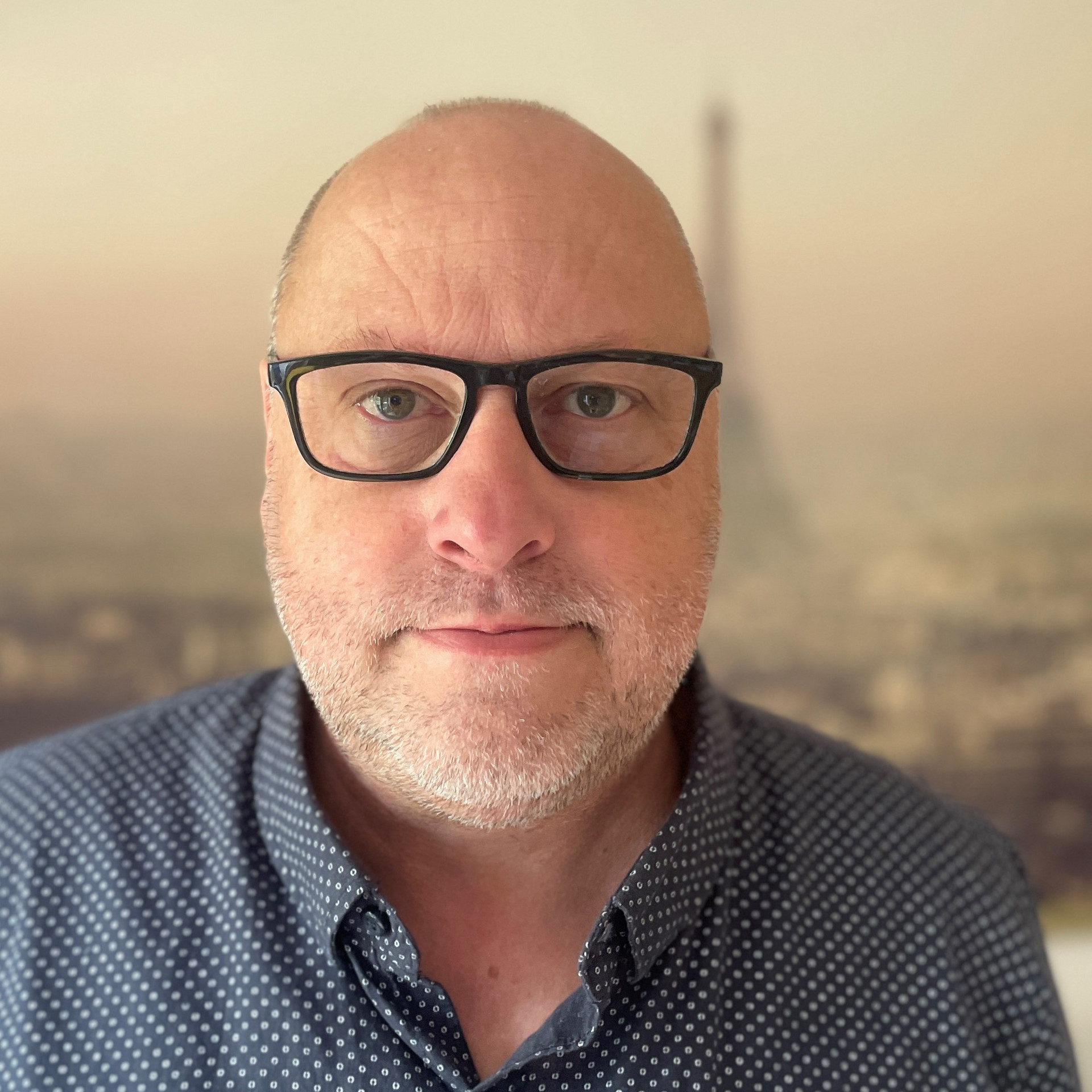Portrait einer Person mit sehr kurzen Haaren, Brille und dunklem Hemd
