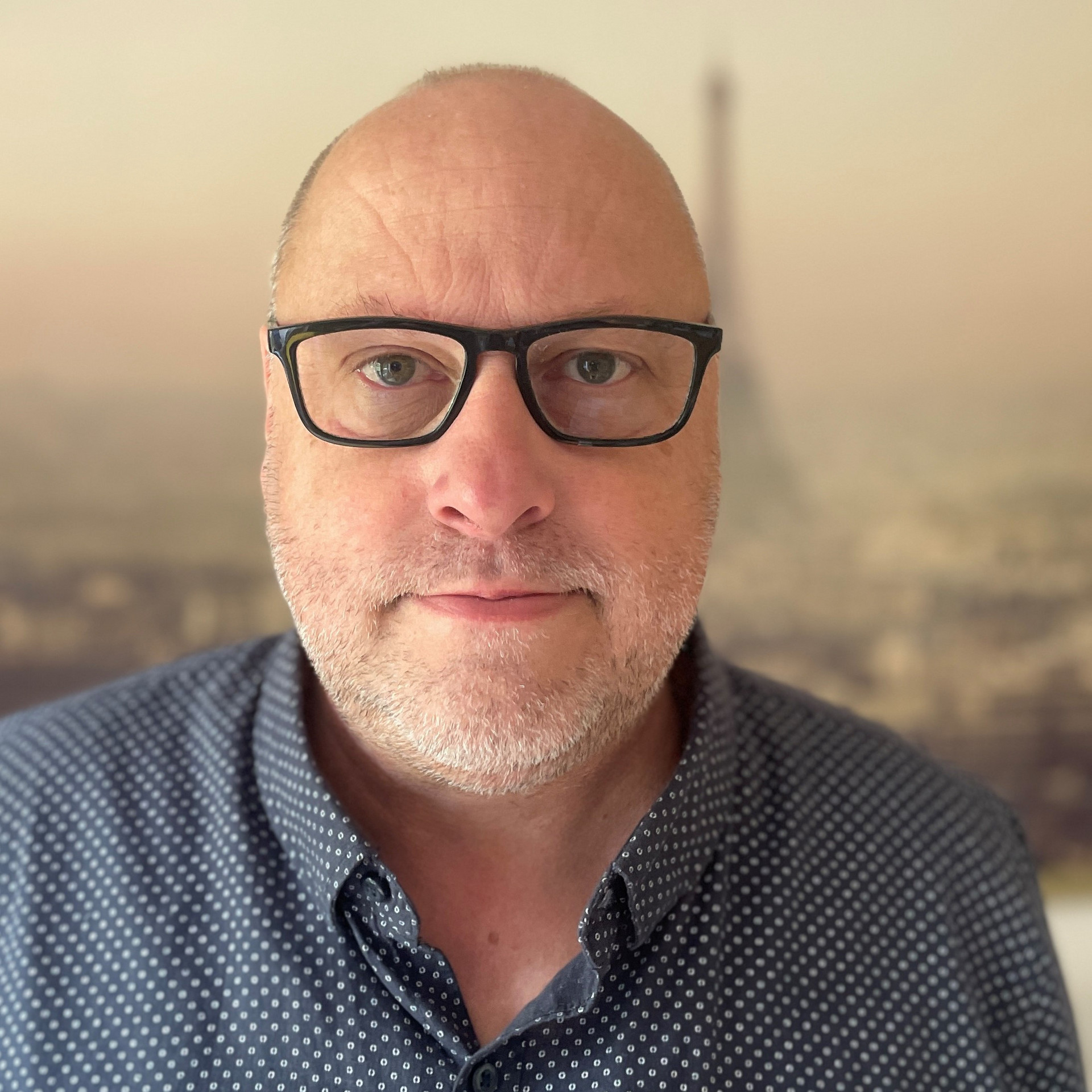 Portrait einer Person mit sehr kurzen Haaren, Brille und dunklem Hemd