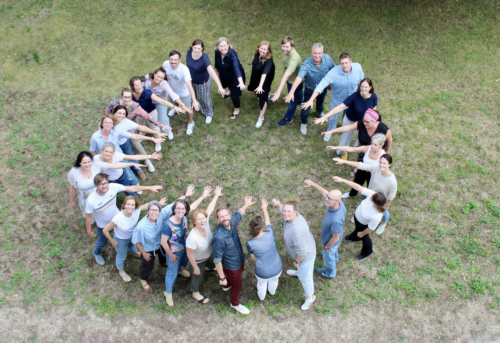 Kollegiumsfoto09/26 Ein Foto des Kollegiums des Studienseminars. Die Fachleitungen stehen im Kreis und halten je eine Hand Richtung Kreismitte.