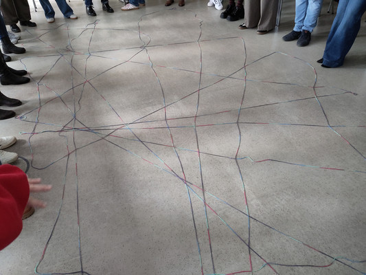 Füße stehen im Kreis. In der Mitte liegt ein Spinnennetz aus bunter Wolle.