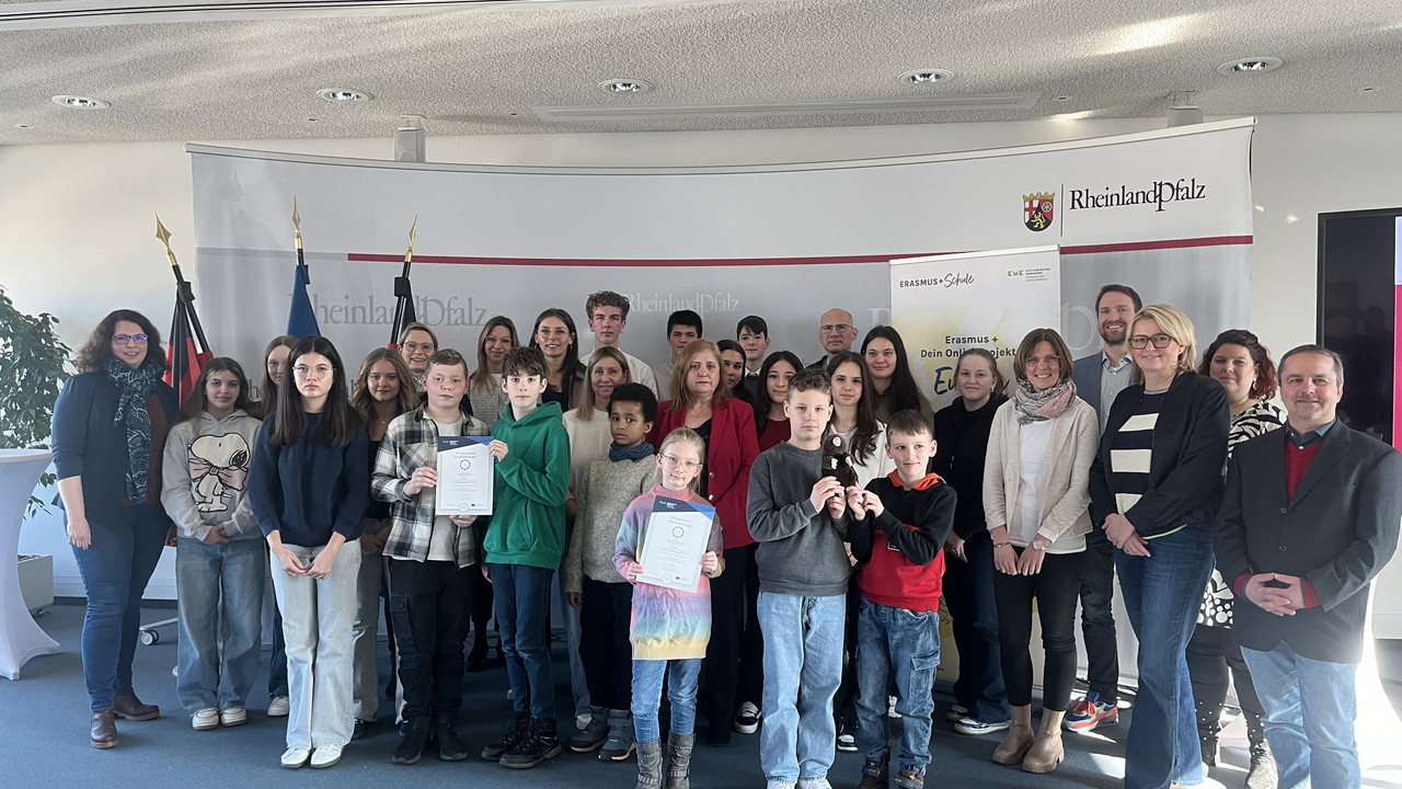 Aufgestellte Gruppe Schülerinnen, Schüler und Erwachsende in einem Raum vor einer Rückwand mit Logo des Bildungsministeriums