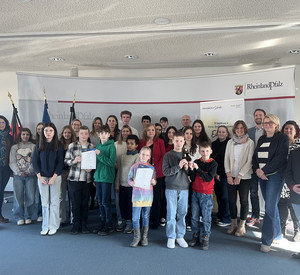 Aufgestellte Gruppe Schülerinnen, Schüler und Erwachsende in einem Raum vor einer Rückwand mit Logo des Bildungsministeriums