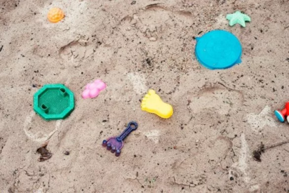 Das Bild zeigt einen Sandkasten.      Im Sand liegen viele bunte Spielzeuge.