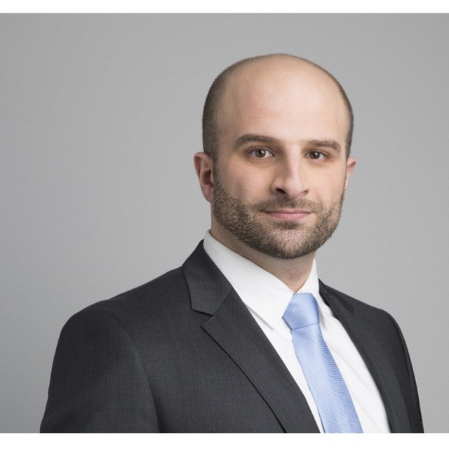 Portraitaufnahme einer Person mit sehr kurzen Haaren, dunklem Jackett, hellem Hemd und Krawatte