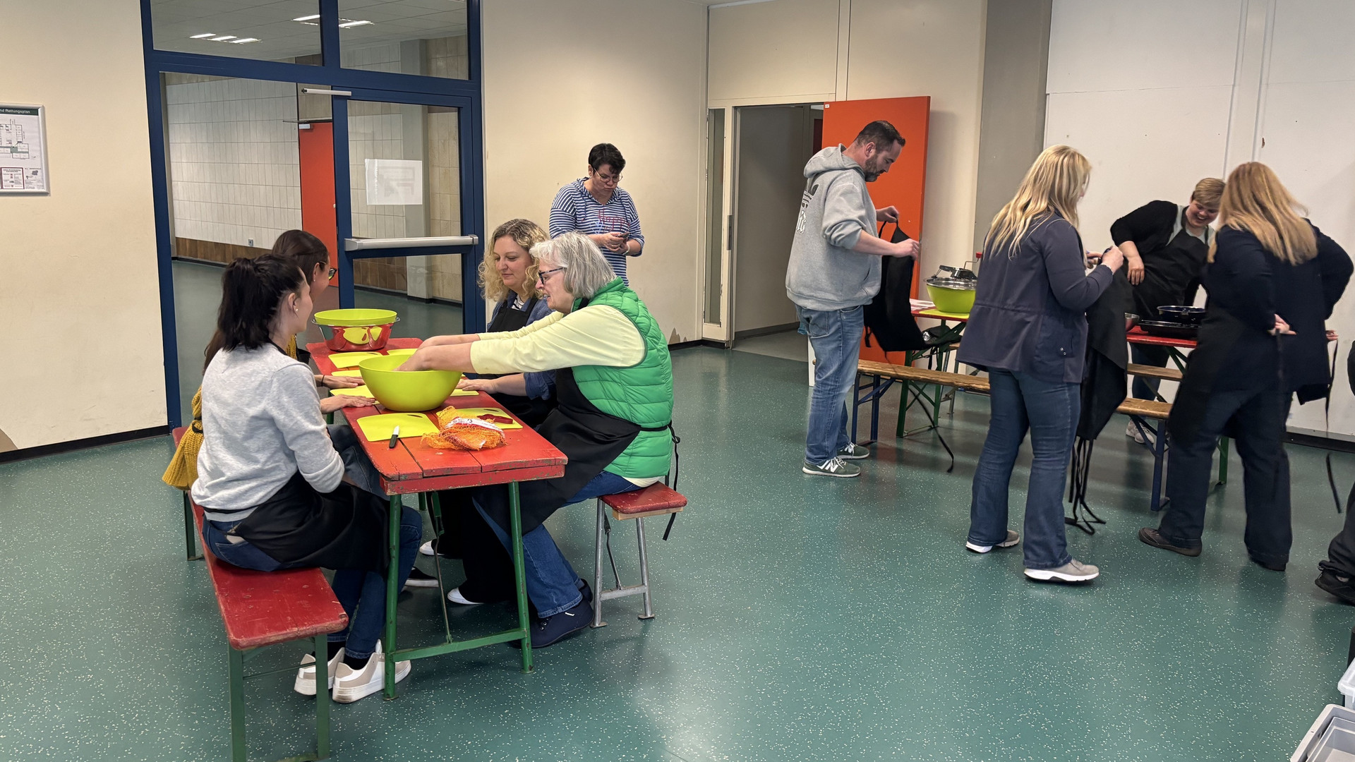 Das Bild zeigt Lehrkräfte, die im Rahmen der Veranstaltung „Der Kochbus kommt” an einem Tisch sitzen und Gemüse für das anschließende Kochen vorbereiten.