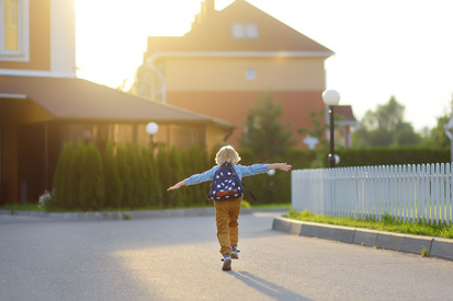 Kleiner Junge mit Rucksack rennt fröhlich eine Straße hinunter.