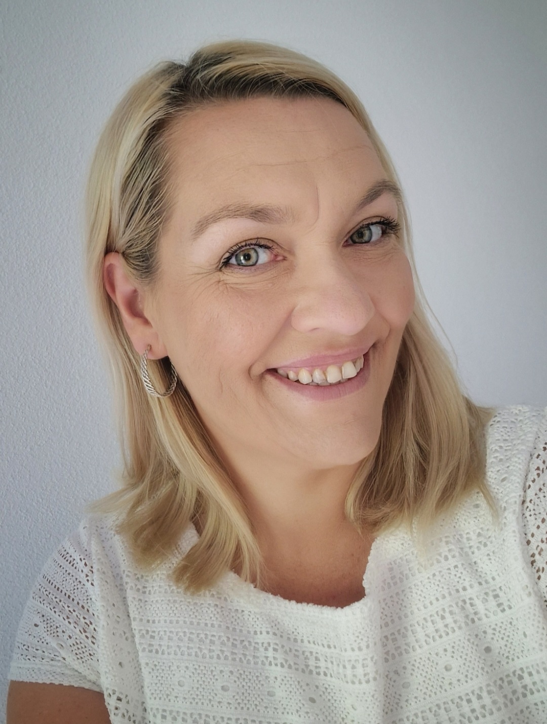 20. LEB_Justyna Winkler Eine Person mit blonden, schulterlangen Haaren und weißem Oberteil, die Person hält den Kopf schräg und lächelt