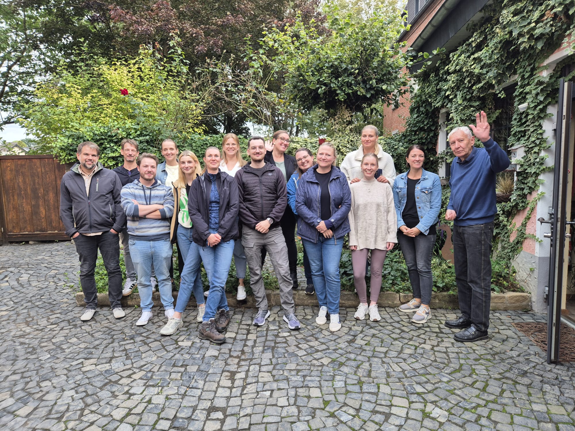 Das Foto zeigt die Teilnehmerinnen und Teilnehmern sowie einem Mieter. Der Mieter grüßt in die Kamera. Die Teilnehmerinnen und Teilnehmer sind sichtlich begeistert von der Wohnform.